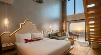 This image shows high ceilings, a king bed, and a private balcony overlooking the ocean at sunset