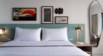 a view of a white bed with two pillows and a bed table with lamp.