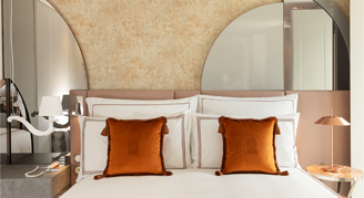Image shows a plush king bed with burnt-orange accent pillows.