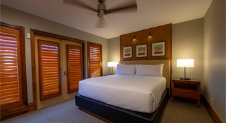 Image shows a king bed with whitle linen and pillows and closed shades.