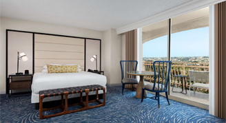 Image shows , featuring a large bed, neutral upholstered wall panels, and a private balcony overlooking the area.