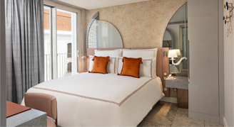 Image shows a plush king bed with burnt-orange accent pillows.