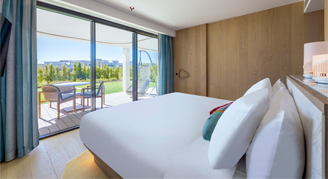 The image shows a plush king-size bed with a private balcony with outdoor seating.