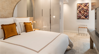 Image shows a plush king bed with burnt-orange accent pillows.