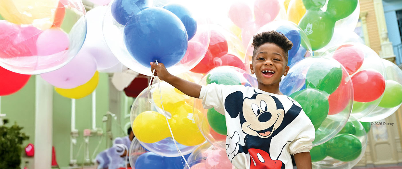 Image a child wearing a Mickey Mouse shirt holding balloons.