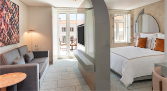 Image shows a plush king bed with burnt-orange accent pillows separating the living room area with a divider wall.