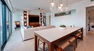 The image shows a family area with a kitchen and dining area in the background and a view outside.