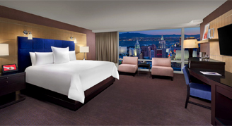 Image shows a king bed with a expansive window view of the city.
