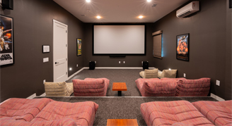 This image shows a tiered home theater room with a projection screen on the far wall and pink seating modules arranged on different levels.