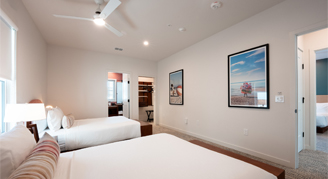 The image shows a bedroom with white walls, a white ceiling fan, and framed artwork hanging on the wall.