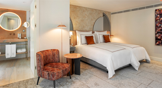 Image shows two twin beds with burnt-orange accent pillows and arm chair.