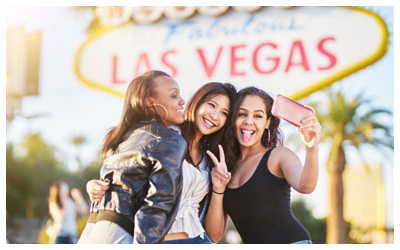 Image is of three friends taking a photo in front of the Las Vegas sign