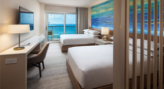 Image of two beds and a work area leading to a balcony in an Infinity Oceanfront Room.