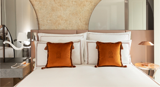 Image shows a plush king bed with burnt-orange accent pillows.