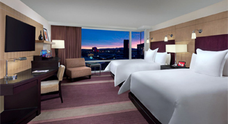 Image shows a two queen beds with a expansive window view of the city.