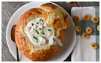 Image of a breadcrumb bowl filled with chowder on a plate with crackers.