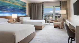 Image of two beds and work area leading to a balcony in a Partial-Ocean-View Room.