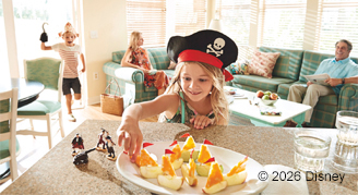 Little girl grabbing a snack off the counter in a pirate costume with family in background on couch
