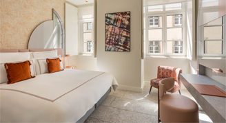 Image shows a plush king bed with burnt-orange accent pillows and desk area.