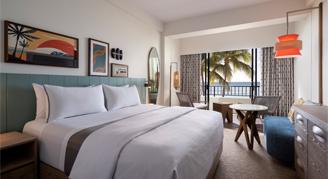 Room with a white bed, desk and chair, and view of ocean