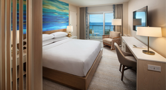 Image of a bed and a work area leading to a balcony in an Infinity Oceanfront Room.