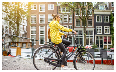 Young woman in yellow raincoat with bag and flowers riding a bicycle in Amsterdam city.