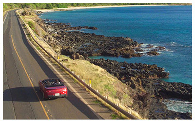 Image of a convertible driving along the coastline in Hawaii.
